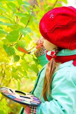 cute little girl is painting autumn leaves outdoorsの写真素材