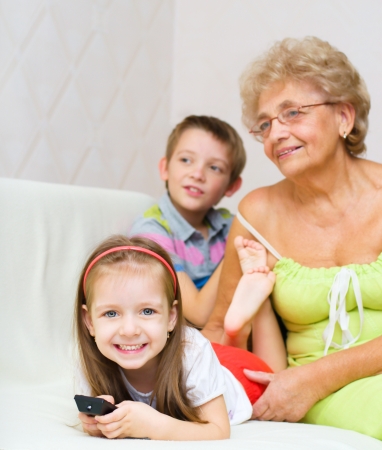 grandmother with her grandchildren are watching TV while sitting on a couchの写真素材