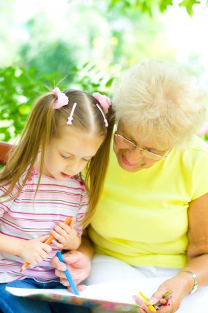 little girl with her grandmother drawing using crayons outdoorsの写真素材
