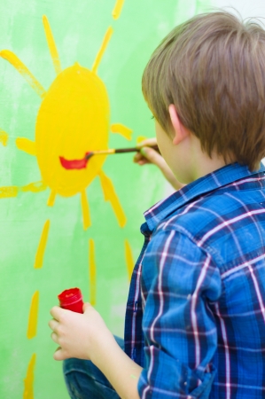 cute boy painting happy sun on the wall at homeの写真素材