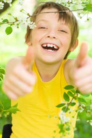 Spring portrait of a happy boy showing thumbs up outdoorsの写真素材