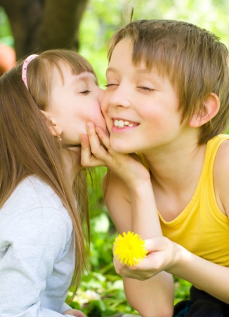 Cute little girl gives her brother a kiss on the cheek outdoorsの写真素材