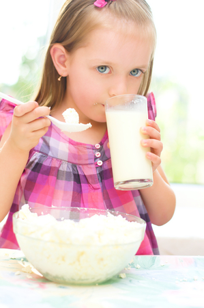 healthy food, child is eating cottage cheese, curd and drinking milkの写真素材