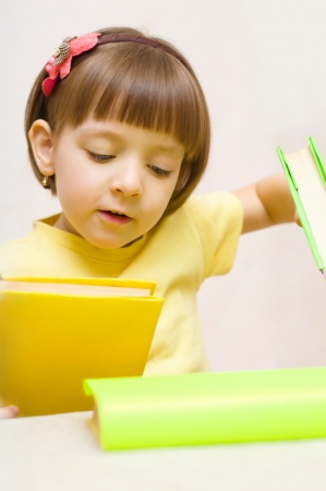 Cute little girl play with books while sitting at tableの写真素材
