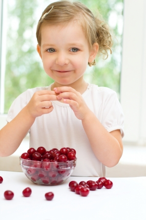 little girl with cherry berries bowl indoorsの写真素材