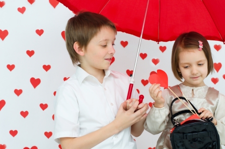 children couple under red umbrella on hearts shapes rainy background for Valentine's Day and other occasionsの写真素材