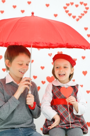 Children couple under red umbrella on hearts shapes rainy background for Valentine's Dayの写真素材
