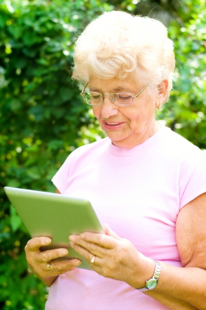 Portrait of an elderly woman working on a tablet and smiling, outdoorsの写真素材