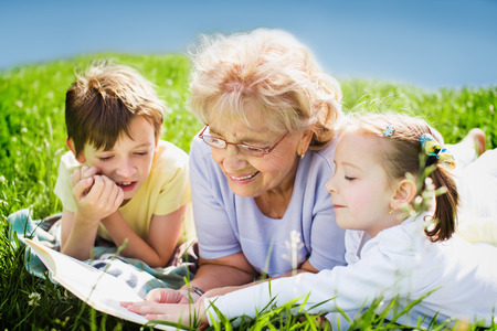 grandmother reading book to grandchildren outdoorsの写真素材