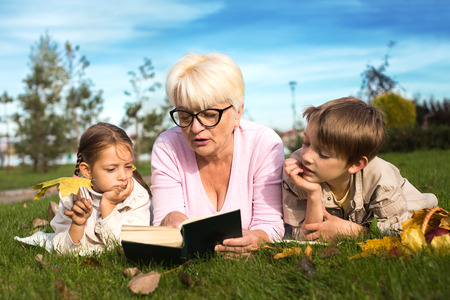 grandmother reading book to grandchildren outdoorsの写真素材