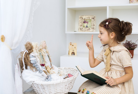 Portrait of a little girl reading book to her textile handmade princess dollsの写真素材