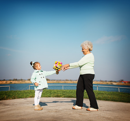 happy granddaughter giving flowers to grandmother outdoorsの写真素材