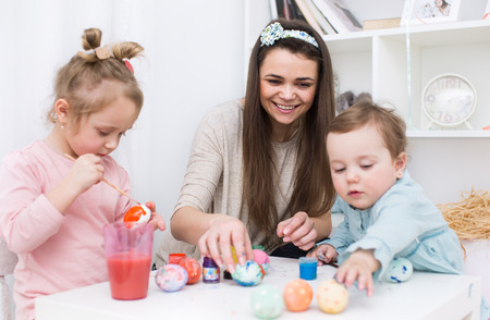 Loving mother and her little daughters painting easter eggsの写真素材