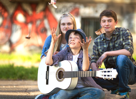 Portrait of happy teens playing the guitar surrounded by  friendsの写真素材