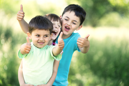 summer portrait of happy children together showing their thumbs up outdoorsの写真素材