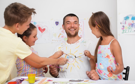 Portrait of a cute happy father with children painting and havinÐ¿ fun. They are showing their hands painted in bright colorsの写真素材