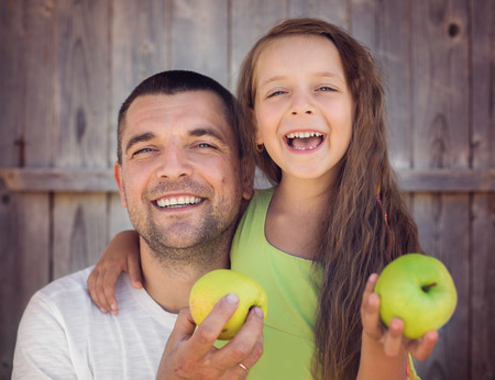 Happy father with daughter holding green apple and smiling outdoorsの写真素材