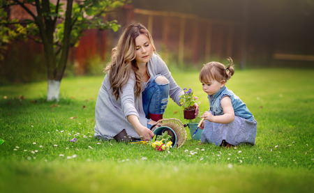 Gardening discovering, family and teaching concept. Happy mothe with little daughter are planting flowers into the groundの写真素材