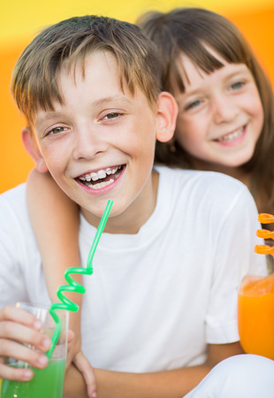 Closeup portrait of cute children drinking orange juice in the summer outdoorsの写真素材