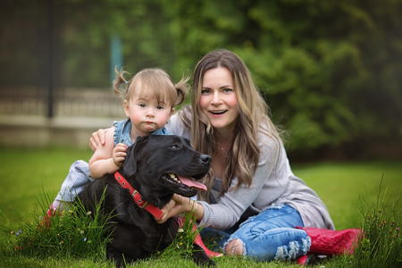 Happy mother with baby playing with dog in green field