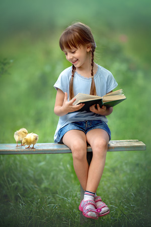 Cute little girl is reading the book with her friends chickensの写真素材