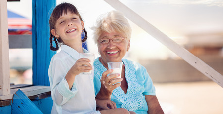 Grandmother with granddaughter drinking milk outdoorsの写真素材