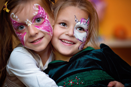 Funny cute little girls with painting faces are hugging ang having funの写真素材