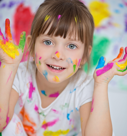 Portrait of a cute cheerful happy little girl showing her hands painted in bright colorsの写真素材