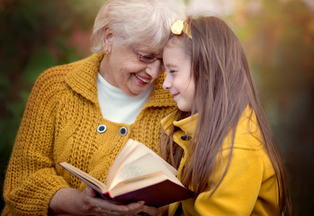 Grandmother with granddaughter reading book in autumn parkの写真素材