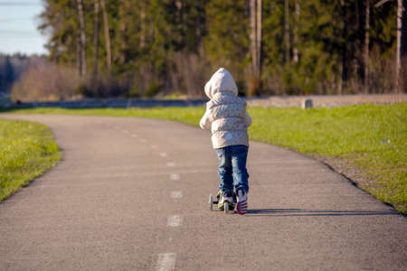 The little girl riding scooter on walking path