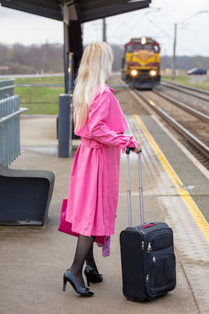 the blonde costs on the platform with a suitcase and waits for the trainの写真素材