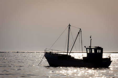 ship silhouette. calm on the sea. small boat on the background of shiny wavesの写真素材