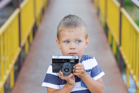 Cute boy with a camera standing on a golden bridge to the outdoors in summerの写真素材
