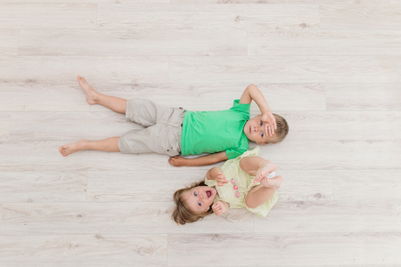 Little boy and girl lying on the floor. Brother and sister playing at home on the floorの写真素材
