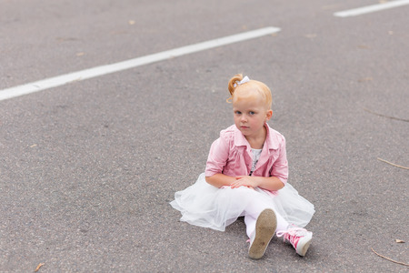 A cute little girl in a beautiful dress and sneakers playing on the road. Redhead girl in the lush dress outdoorsの写真素材