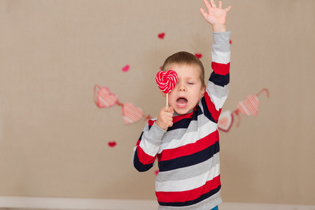 Portrait of a beautiful boy in a striped sweater and jeans. The boy with blue eyes with a candy in the handsの写真素材
