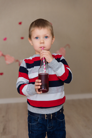 Portrait of a beautiful boy in a striped sweater and jeans. The boy with blue eyes with a juice in the handsの写真素材