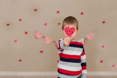 Portrait of a beautiful boy in a striped sweater and jeans. The boy with blue eyes with a candy in the handsの写真素材