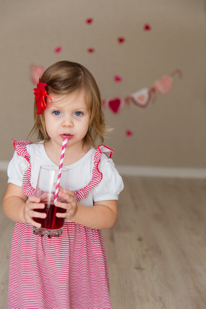 Little cute girl on the background wall of a house. The child in the scenery in the form of hearts. The kid drinks juiceの写真素材