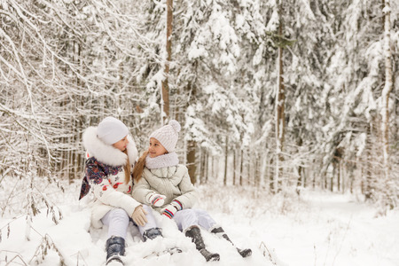 Two girlfriends playing in a winter forest. The sisters have a rest in the open air in winterの写真素材