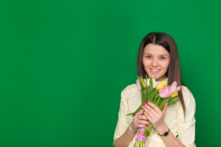 Beautiful girl with a bouquet of tulips on a green background in the studioの写真素材