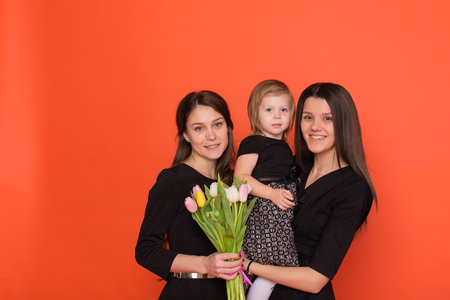 Beautiful sister with a bouquet of flowers on a red background in studioの写真素材