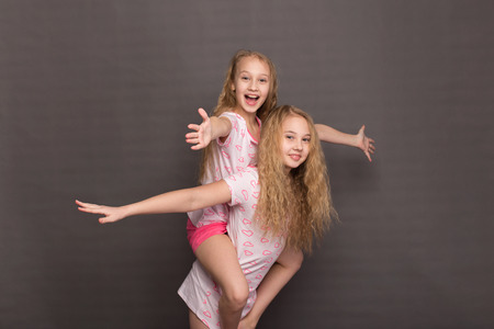 Beautiful two girls in pink pajamas play before going to bed. Sisters in pajamas are getting ready for bed. Fighting with pillows before bedtimeの写真素材