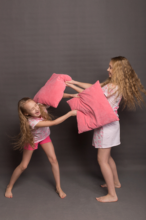Beautiful two girls in pink pajamas play before going to bed. Sisters in pajamas are getting ready for bed. Fighting with pillows before bedtimeの写真素材