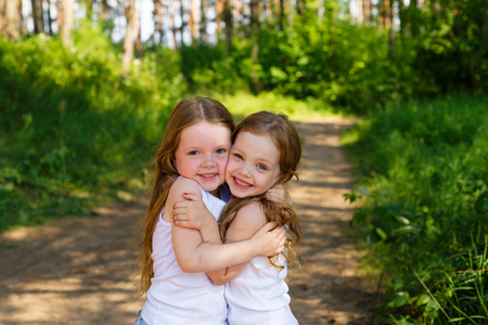 Two little girl girl friends hugging in the forest on a sunny afternoonの写真素材