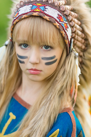 Beautiful young girl in the image of an Indian with a roucche on her head and a bow with arrows in...
