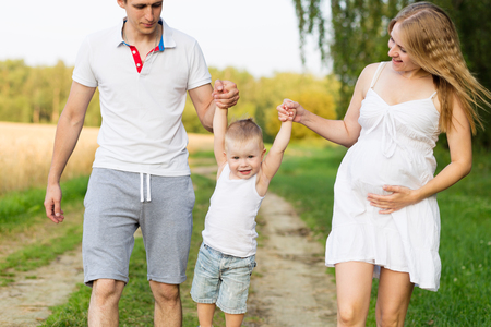 A young family with a small boy waiting for a second child. Future parents with a child outdoors in summerの写真素材