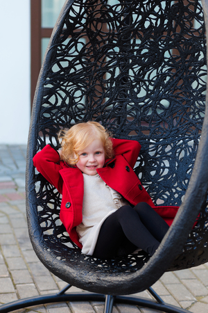 Portrait of a beautiful little girl with red hair in a red coat outdoors in springの写真素材