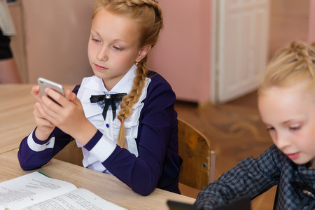 Girls at school desks. Girlfriends are sitting at school with books, notebooks and telephones. Children study in the school roomの写真素材