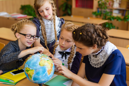Girls at school desks. Girlfriends are sitting at school with books, notebooks and telephones. Children study in the school roomの写真素材